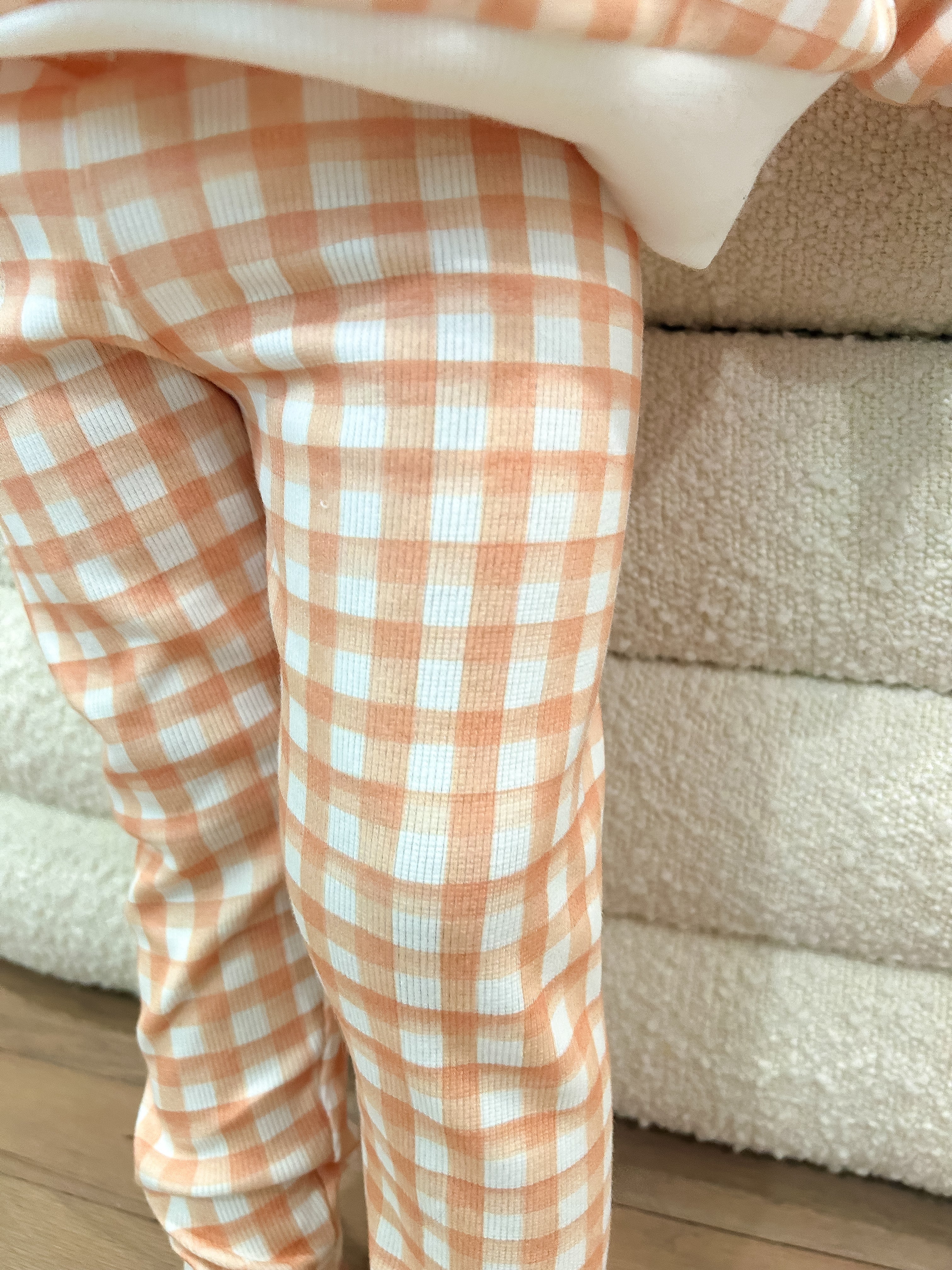 Toddler wearing orange and white checkered pants standing in front of a sherpa ottoman.
