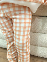 Toddler wearing orange and white checkered pants standing in front of a sherpa ottoman.