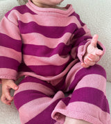 Child wearing a pink and purple striped outfit on a neutral background