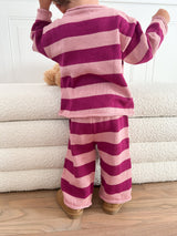 Toddler wearing pink and purple striped pajama standing on a wooden floor.