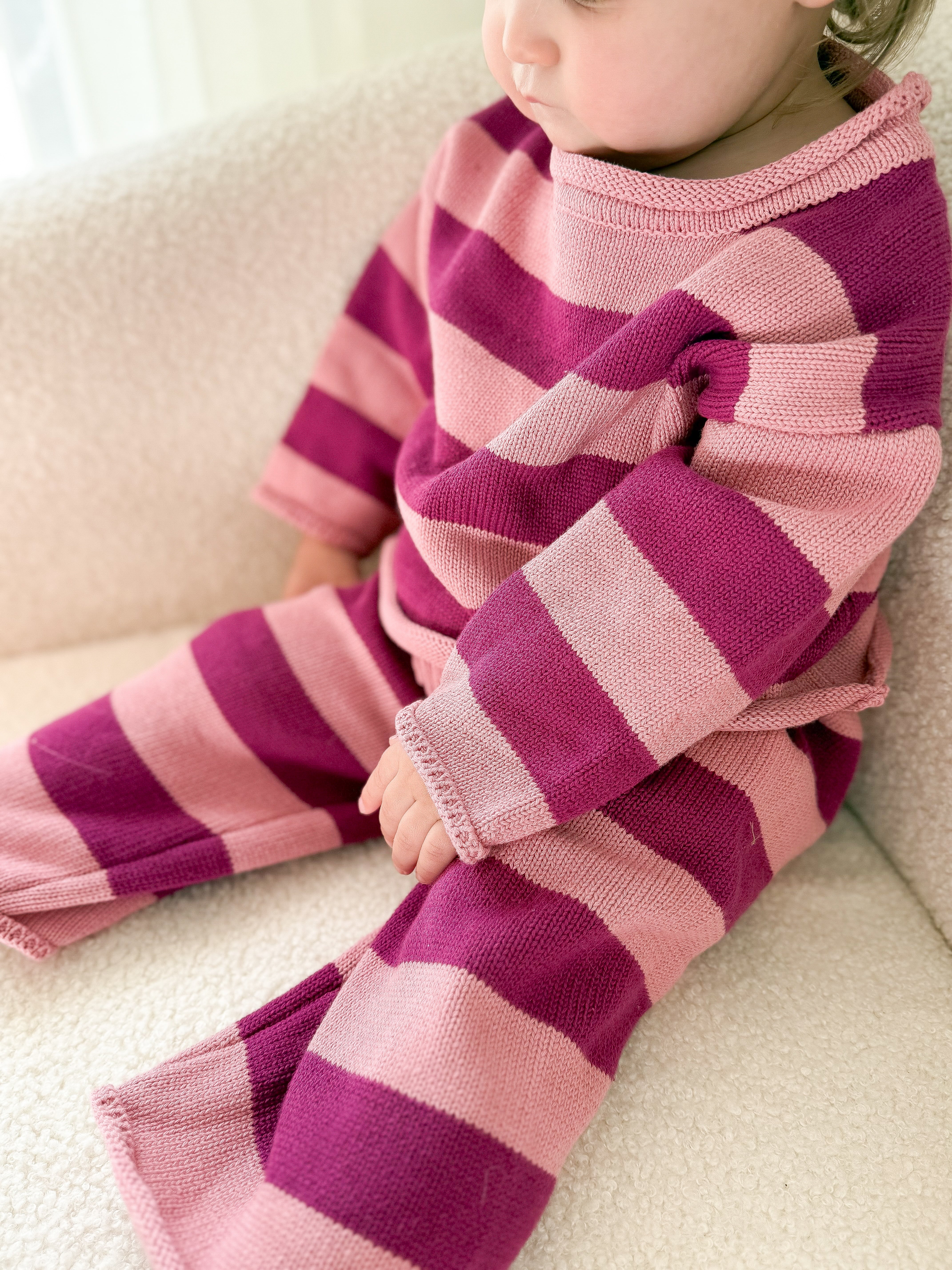 Toddler wearing pink and purple striped set sitting on a sherpa surface.