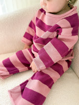 Toddler wearing pink and purple striped set sitting on a sherpa surface.