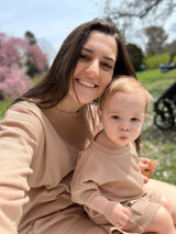 A mom wearing a long sleeve beige waffle top and shorts set and son sitting on lap wearing a matching beige waffle short sleeve outfit set, with cherry blossoms in the background.
