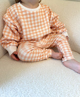 Toddler wearing an orange and white checkered outfit sitting on a beige sherpa chair.