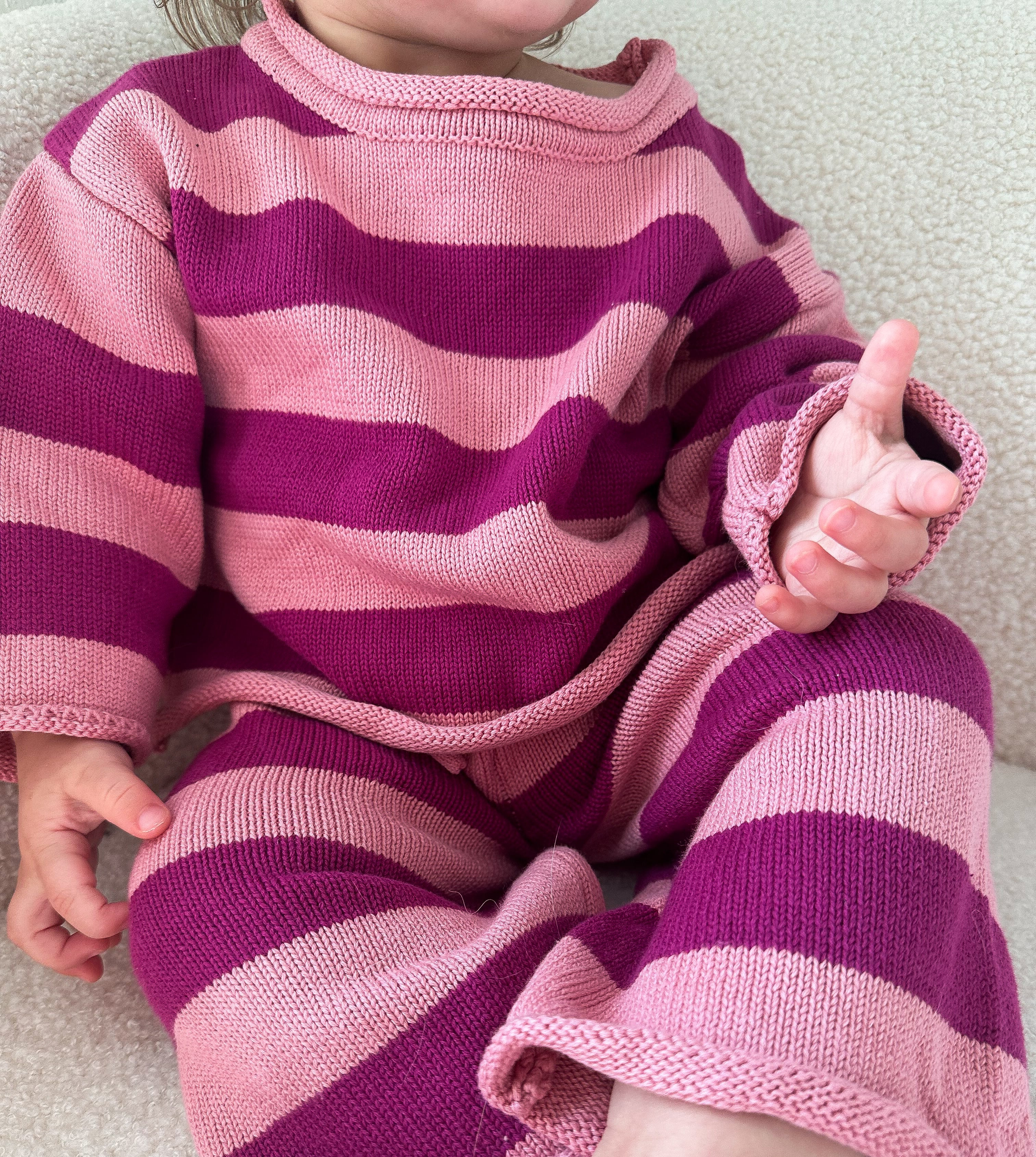 Child wearing a pink and purple striped outfit on a neutral background