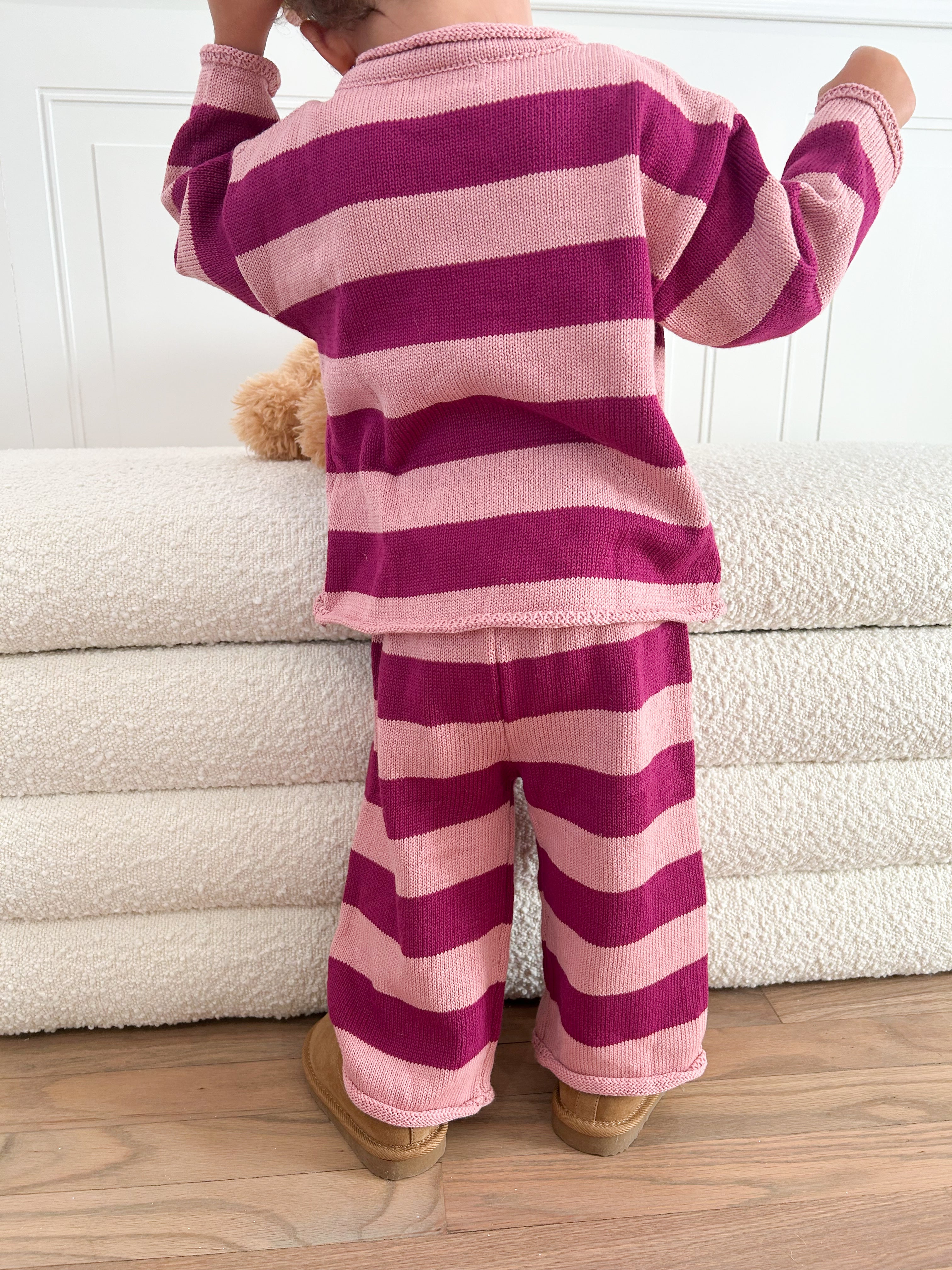 Toddler wearing pink and purple striped pajama standing on a wooden floor.