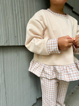 a child wearing a beige sweater and plaid pants