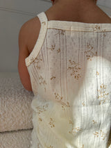 Close-up of a baby wearing a white tank top with floral pattern on neutral background.