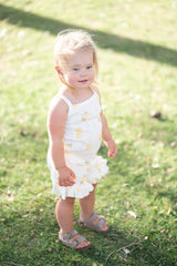 Toddler in a lemon outfit set standing on grass smiling.