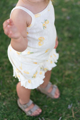 Child wearing a white outfit set with lemons standing on grass. Cropped so only outfit is shown.