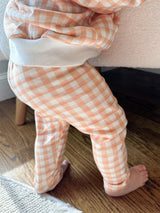 Toddler wearing orange gingham pants standing on a wooden floor