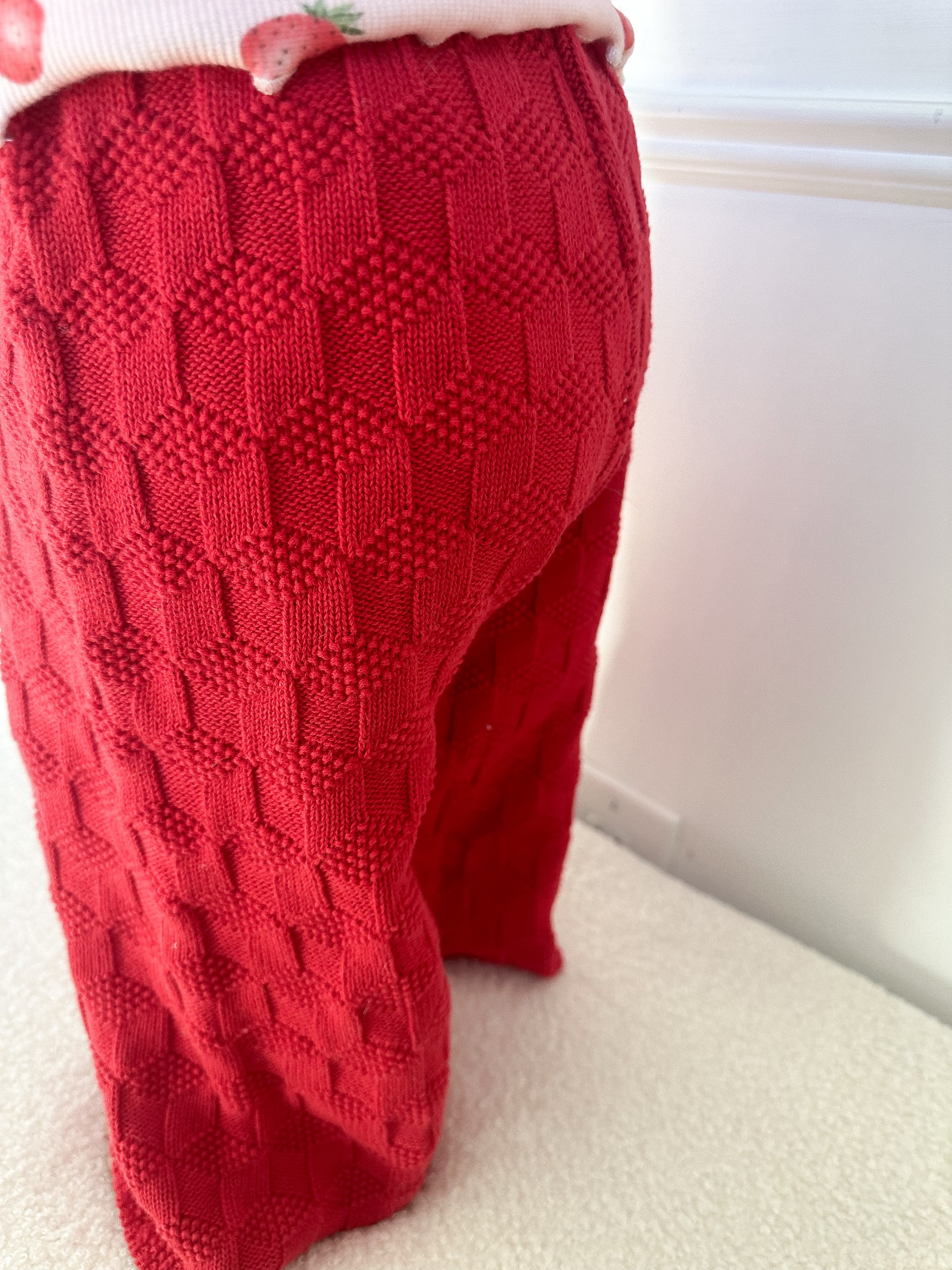 Red textured pants worn by a child standing on a white surface. Cropped to only show pants.