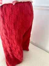 Red textured pants worn by a child standing on a white surface. Cropped to only show pants.