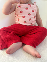 Child wearing a pink tank top with strawberry pattern and dark pink knitted pants sitting on a light-colored surface. Cropped to only show outfit.