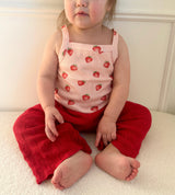 Child wearing a strawberry-patterned top and dark pink knitted pants sitting on a white surface. Cropped to only show part of face and outfit.