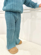 Toddler wearing a blue checkered outfit with slippers on a white background