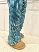 Blue checkered pants worn with brown slippers on a white background