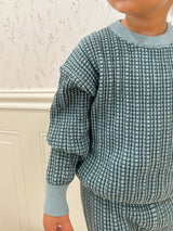 Child wearing a blue checkered outfit against a neutral background