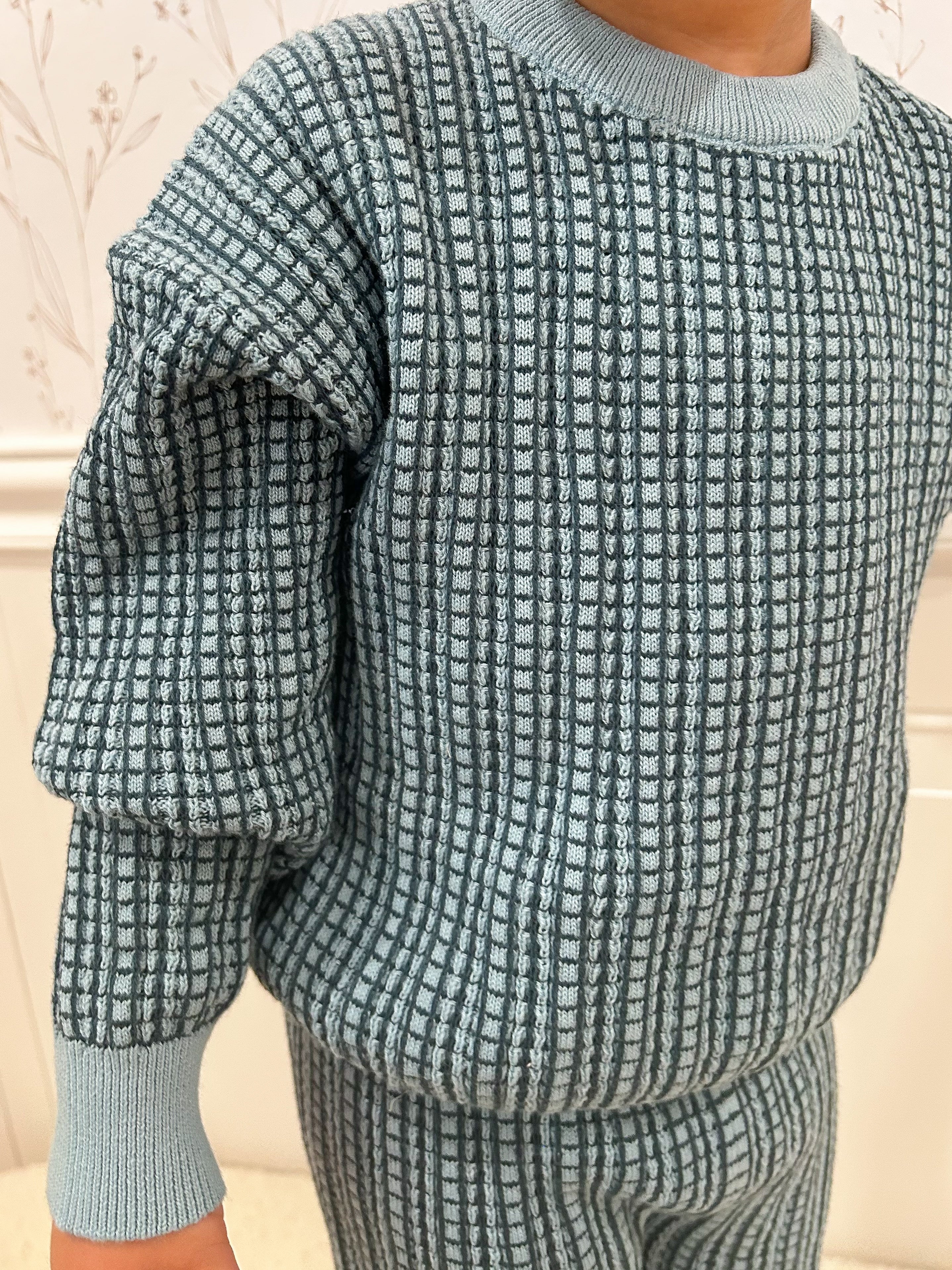Blue and navy checkered sweater worn by a child against a light background. Cropped to only show sweater.