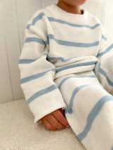 Child in a bright room wearing a white and blue striped sweater and pants sitting on a light-colored surface.