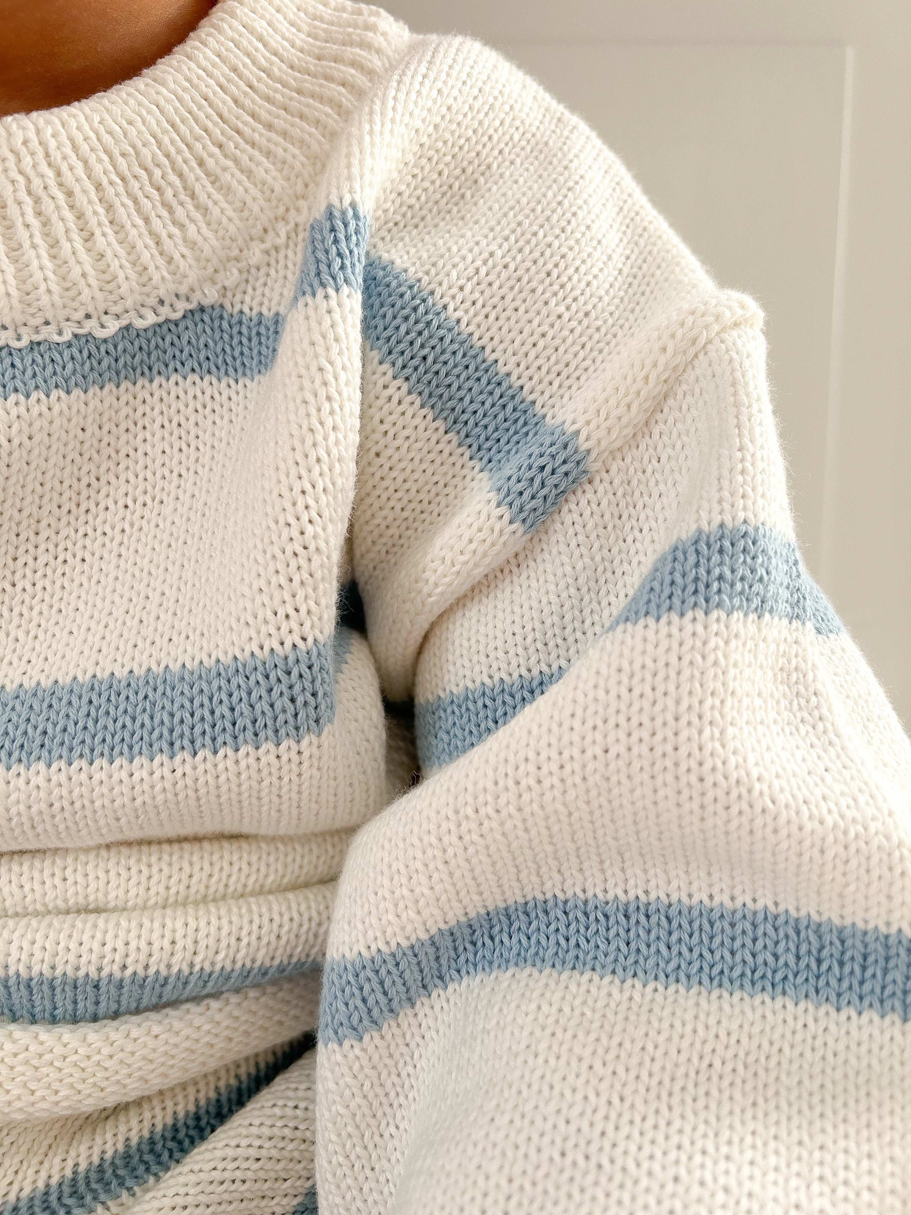 Close-up of a white sweater with blue stripes on a neutral background.