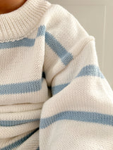 Close-up of a white sweater with blue stripes on a neutral background.