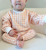 Toddler wearing an orange and white checkered outfit sitting on a  beige sherpa chair.