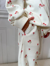White baby sweat set with red floral patterns worn by a child, against a neutral background. Childs hand is in pocket.