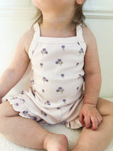 Child wearing a light-purple tank top with floral pattern and matching shorts with ruffle trim sitting on a light-colored surface.