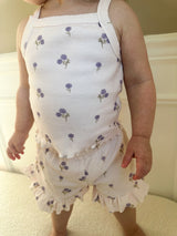 Child wearing a light purple tank set with purple florals with matching shorts with ruffle trim standing on a light-colored surface. 