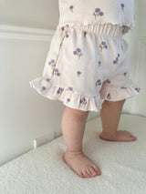 Child wearing light-purple shorts with floral pattern and ruffle trim standing on light-colored surface.